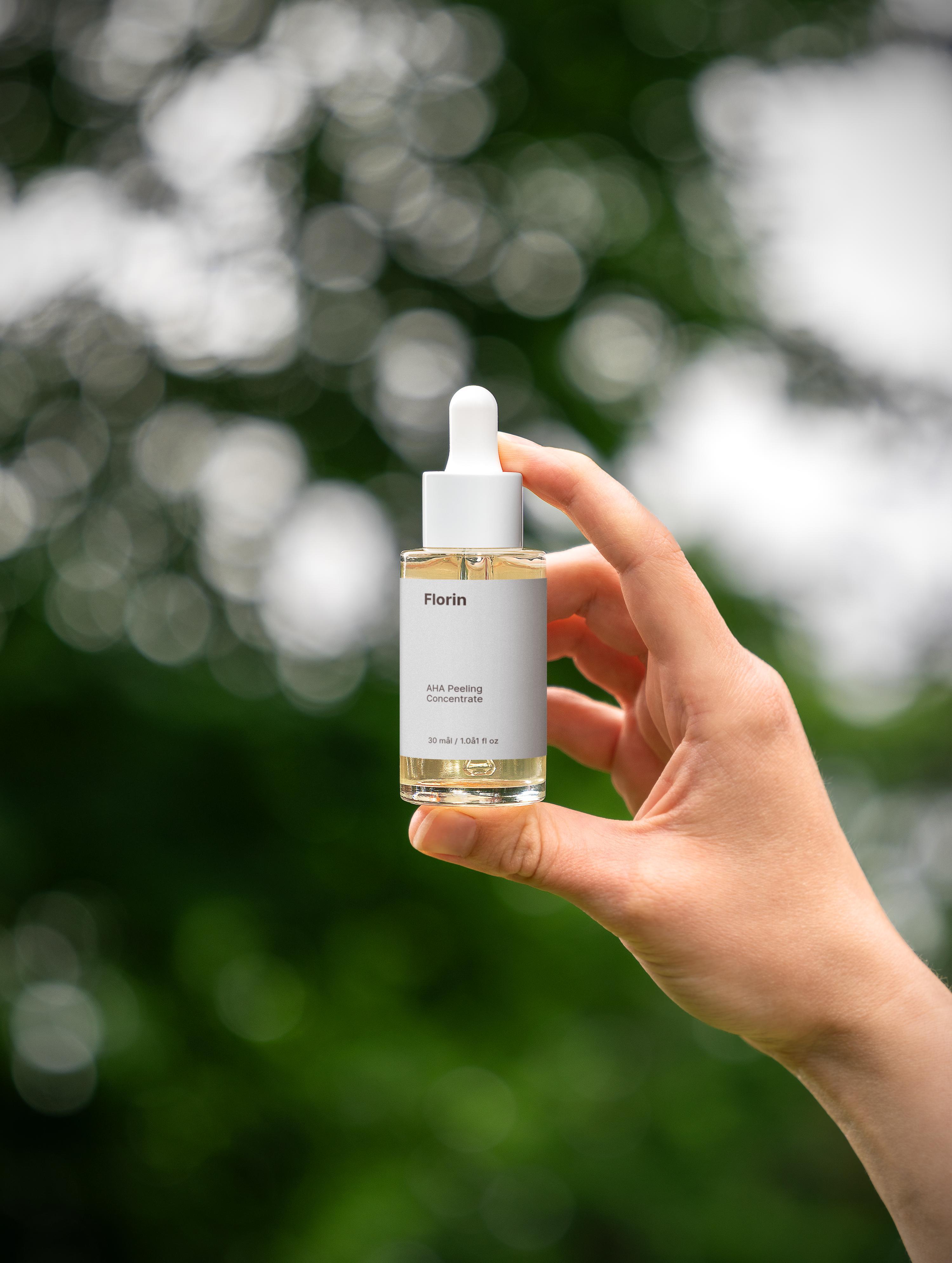Hand holding a skincare serum bottle with a blurred green background